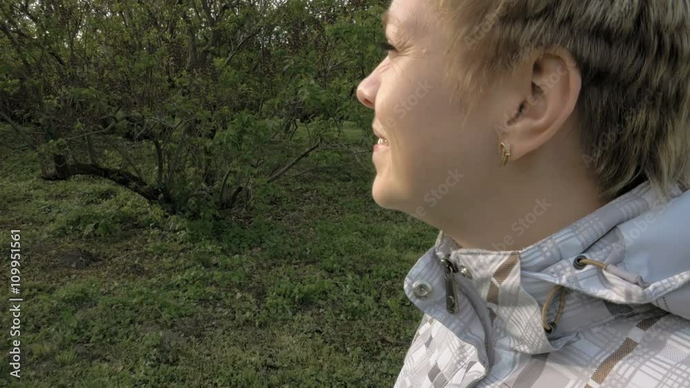 Pretty blond short hair woman closeup portrait outdoors in the green park in spring. Girl looks at the sunset smiles and narrows and squints from the sun. 4K UHD video footage. Pretty blond short hair woman closeup portrait outdoors in the green park in spring. Girl looks at the sunset smiles and narrows and squints from the sun. 4K UHD video footage.
