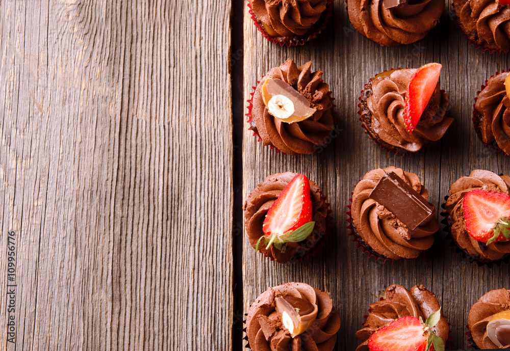 Chocolate cupcakes with strawberry and chocolate on a woodenrustic table. Top view. Chocolate cupcakes with strawberry and chocolate on a woodenrustic table. Top view.