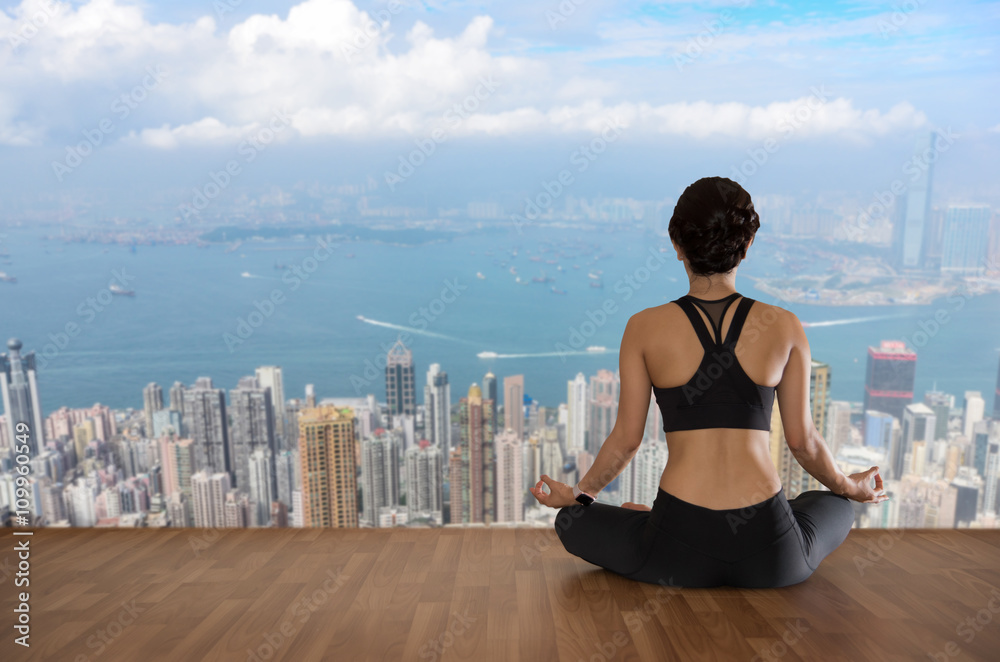 Fototapeta premium young woman practicing yoga meditation on wooden floor with city
