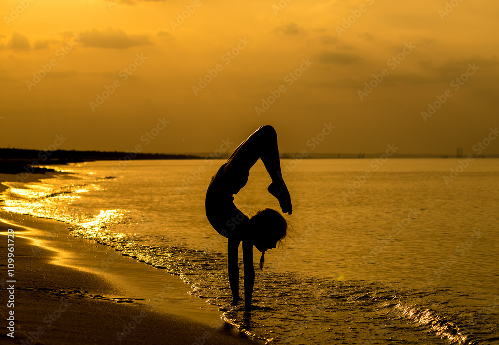 Młoda gimnastyczka nad brzegiem morza w promieniach zachodzącego słońca - obrazy, fototapety, plakaty 