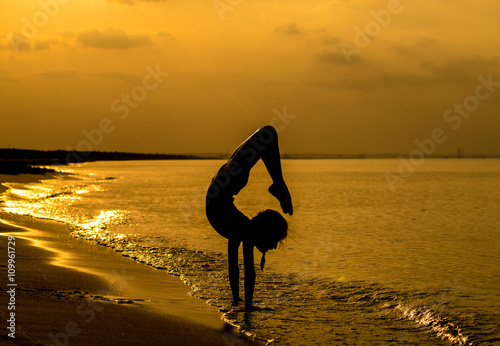 Młoda gimnastyczka nad brzegiem morza w promieniach zachodzącego słońca