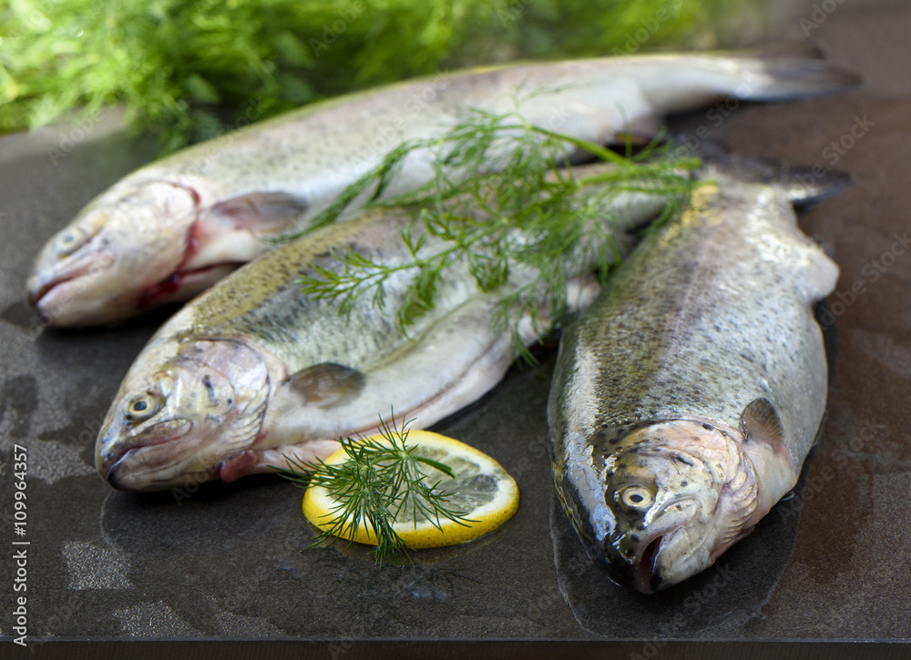 Three rainbow trout on a board, with herbs and lemon, ready for cooking. Three rainbow trout on a board, with herbs and lemon, ready for cooking.