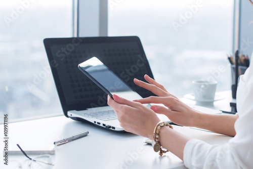 Young woman holding modern tablet computer, using device at workplace during break, chatting, blogging and posting information with apps. photo
