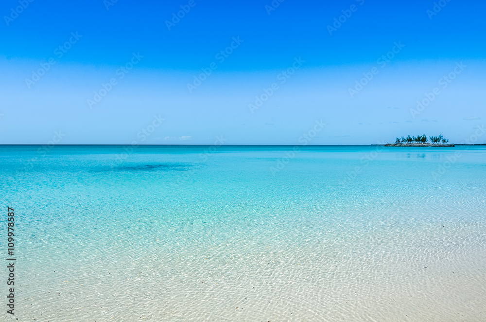 Turquoise, crystal clear water and a small island in the background on Eleuthera (Bahamas).