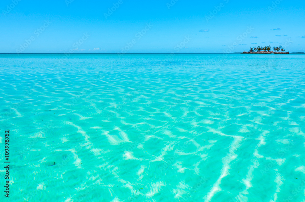 Turquoise, crystal clear water and a small island in the background on Eleuthera (Bahamas).
