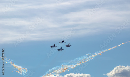 Fototapeta Naklejka Na Ścianę i Meble -  Flight groups of four fighter jets at an air show on a blue sky background, clouds, and thermal rocket plumes.