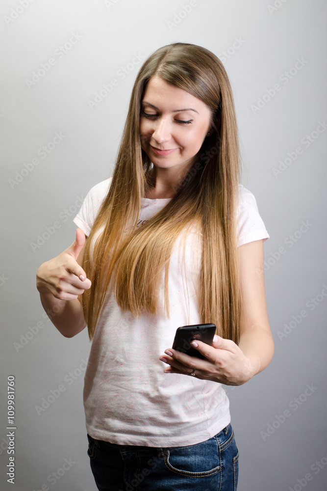 Portrait of an attractive happy brunette young woman pointing to her smart mobile phone, on grey background Portrait of an attractive happy brunette young woman pointing to her smart mobile phone, on grey background