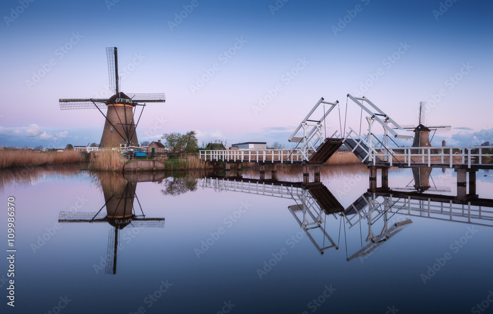 Spring landscape with beautiful traditional dutch windmills near the water channels with drawbridge and reflection in water at sunrise in famous Kinderdijk, Netherlands
