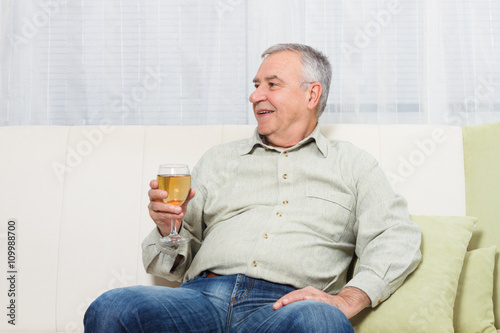 Senior man enjoys drinking wine at home.