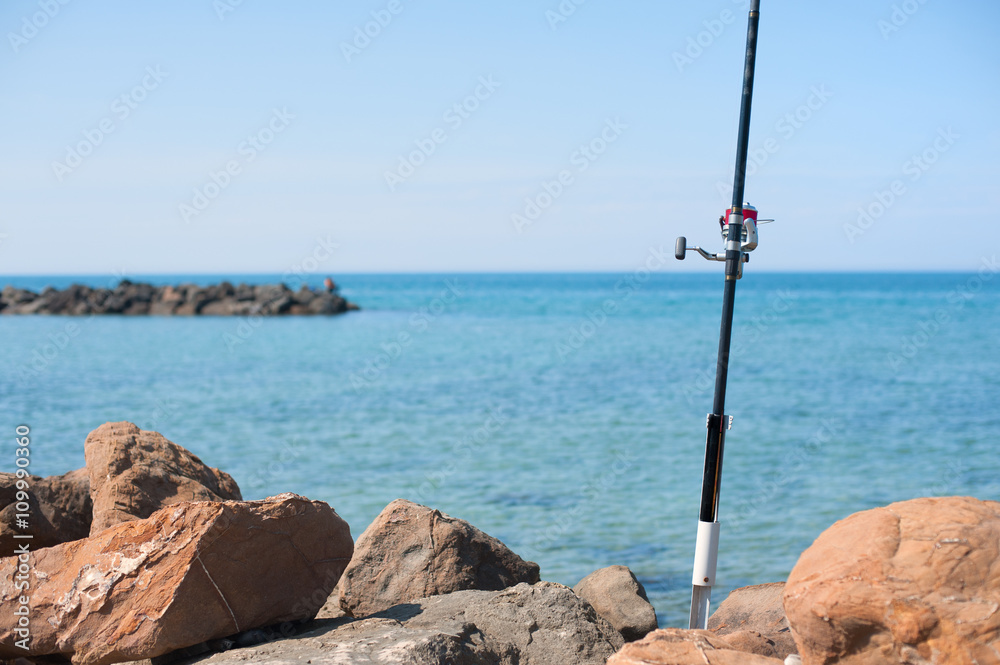 Fishing pole with red reel on blue sea Fishing pole with red reel on blue sea