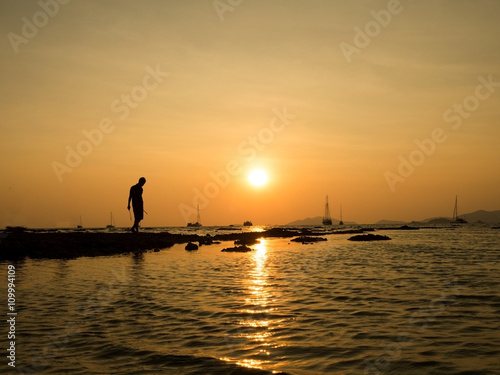 Silhouette of young man standing at sea beach with beautiful sky sunset background.
