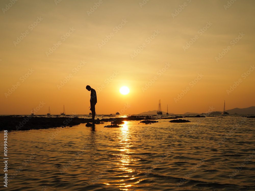 Silhouette of sad young man standing dejectedly turn back to the sun at sea beach with beautiful sky sunset background.