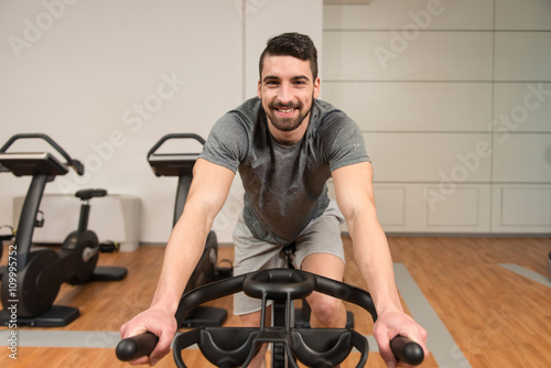 Muscular Man Doing Cycling In Modern Fitness Center