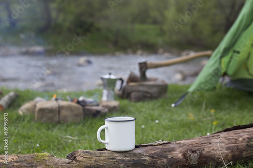Mug stands on a log near the fire at a campsite.
