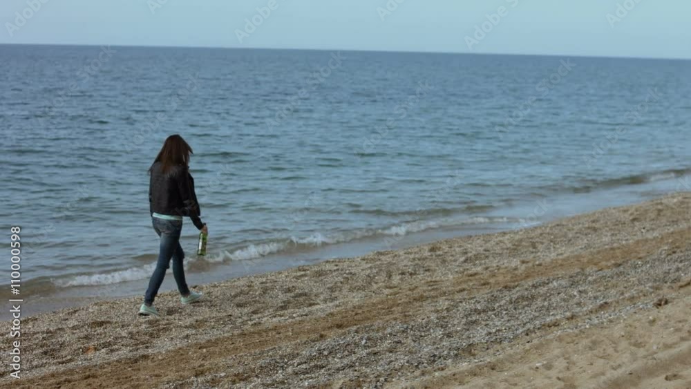 Lonely woman walking on the beach with a bottle of wine Lonely woman walking on the beach with a bottle of wine