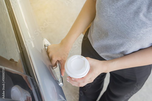 Woman holding white coffee cup and opening a car door, morning w