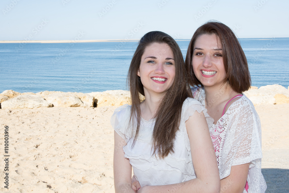Happy young friends sitting by the sea smiling Happy young friends sitting by the sea smiling