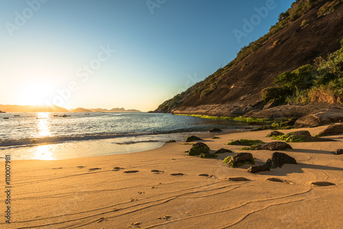 Sunrise in the Beach with Rock and Footsteps in Sand