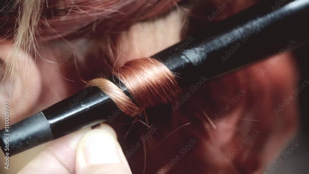 Close-up of a male hairdresser making curls at copper hair with curling irons