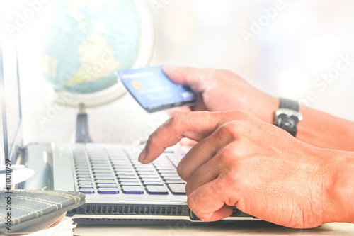 man using computer notebook laptop for shopping online with credit card globe model background selective focus at front hand ,global e-commerce concept