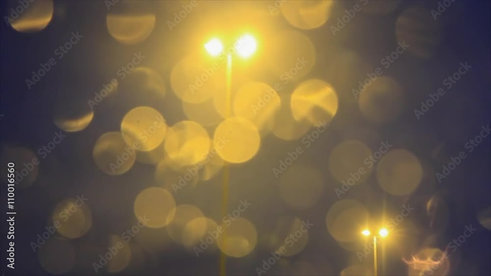 Traveling de farolas de iluminacion en carretera, tras la luna delantera del coche en movimiento ,con reflejos en las gotas de agua de lluvia en tono amarillento, al anochecer

