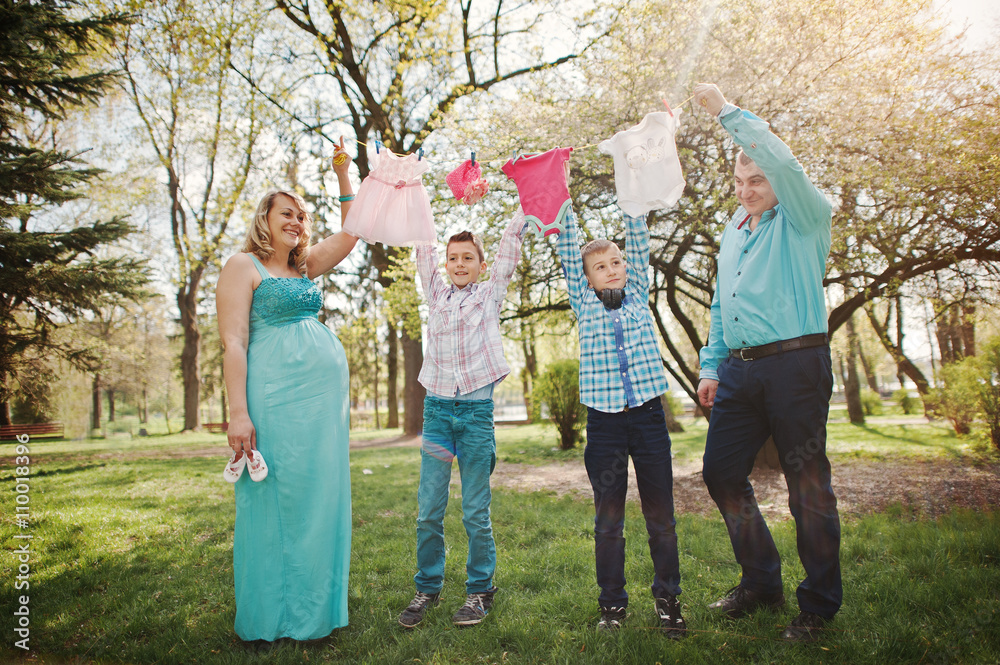 Fototapeta premium Happy pregnant couple with two sons holding girls' baby clothes