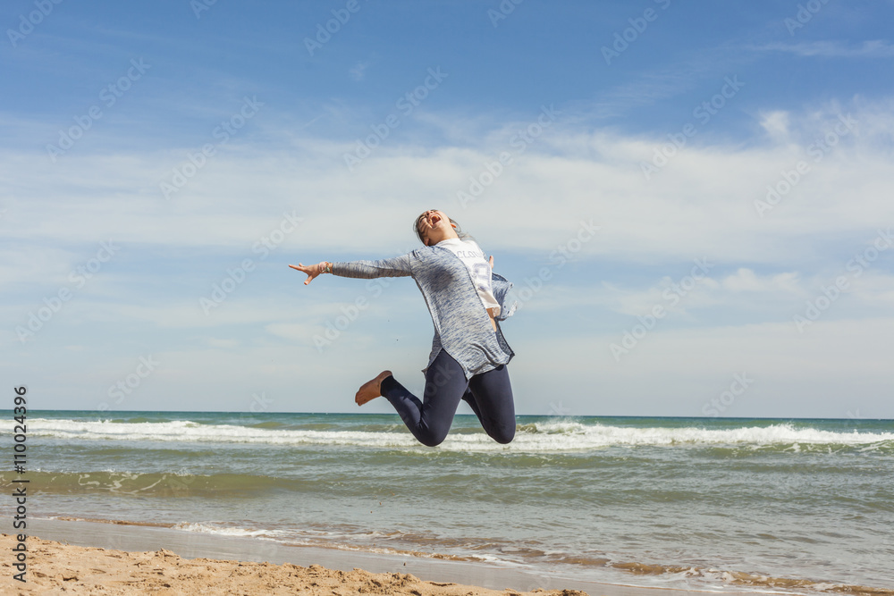 Full shot of a smily teenager jumping in the seashore of the bea Full shot of a smily teenager jumping in the seashore of the bea