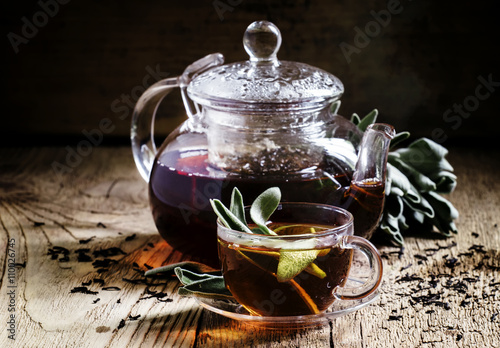 Black tea with fresh sage, glass cup and teapot, dark wood backg