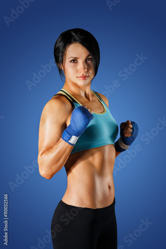 Young sportive woman with dumbbells at blue background