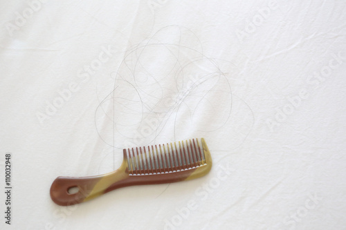 Comb and black hair of women placed on white cloth.