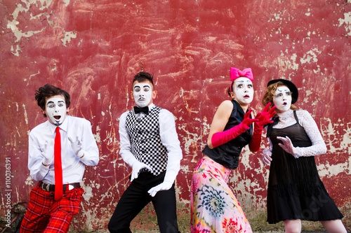 Four mimes standing in awe at the background of a red wall.