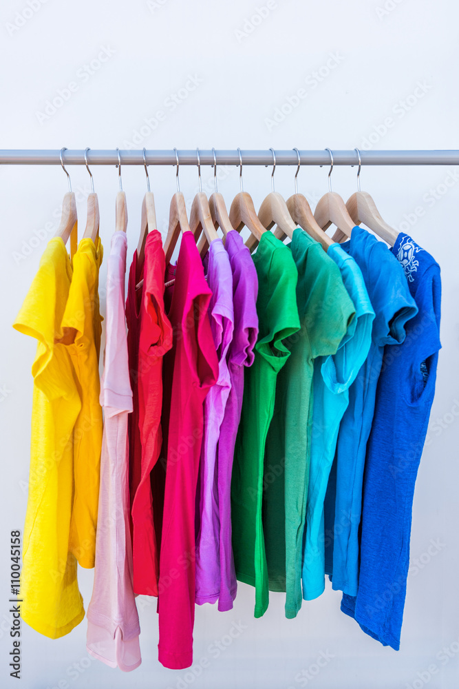 Fashion clothes on clothing rack - bright colorful stand of rainbow  selection of t-shirts. Choice of trendy female wear on hangers in store  closet or spring cleaning concept. Summer home wardrobe. Stock