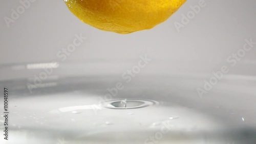 Macro view of drop of water dripping from the fresh yellow lemon on the water surface with little waing splash. White background isolated shooting in super slow motion mode. photo