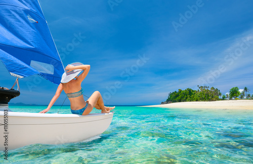 Woman traveler sit at the stern of sailboat looking to the beach