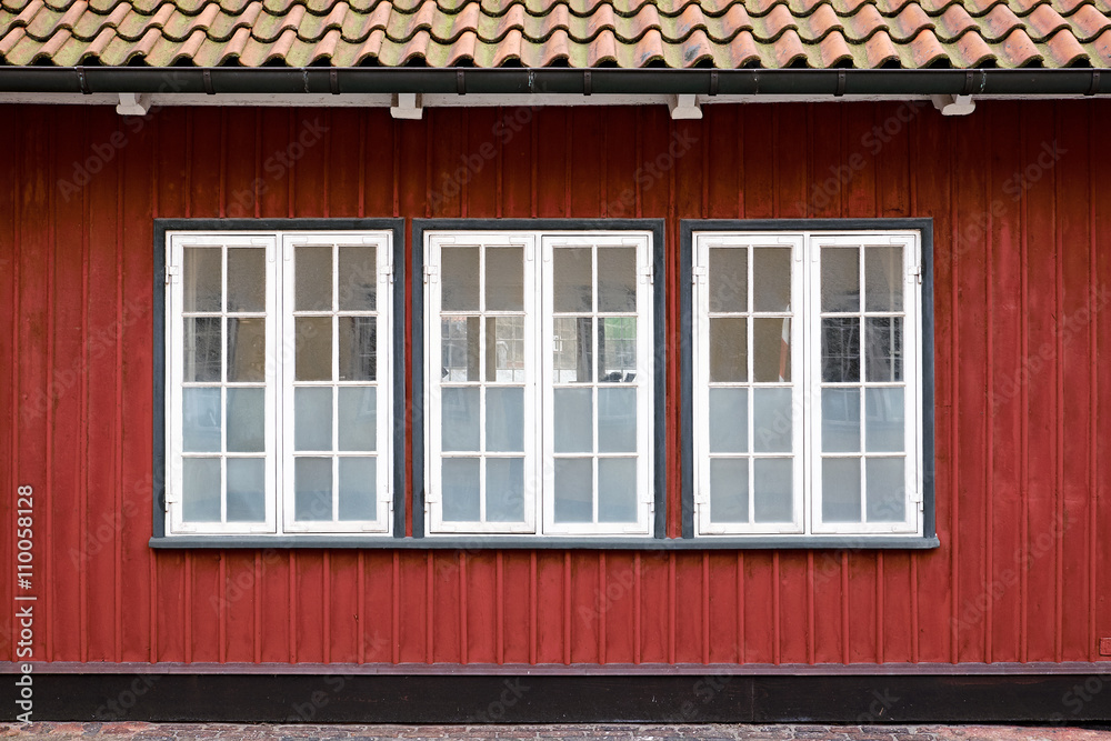 Three white painted casement windows with partly frosted glazing, in a red painted wood plank facade