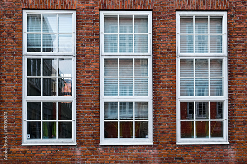 Three tall, white painted, wood windows in a red masonry brick facade