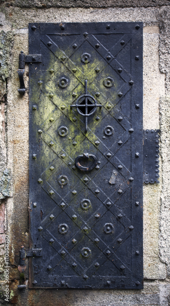 Historical house door. Big metallic old door. One timber leaf, closed black gateway with metal and nails. Exterior country situation. Rural entry architecture element. Village foundation background. Historical house door. Big metallic old door. One timber leaf, closed black gateway with metal and nails. Exterior country situation. Rural entry architecture element. Village foundation background.