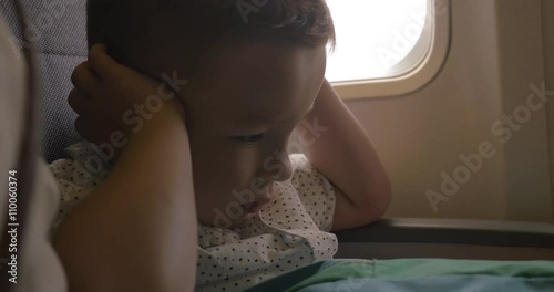 Nervous little child sitting at the airplane and covering ears with hands because of jet loud noise and fright photo