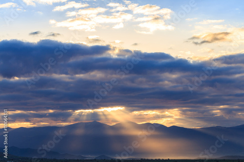 Sunrays light through colorful clouds on rural landscape