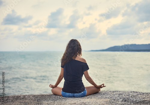 Woman meditating on rocky cliff with sea view