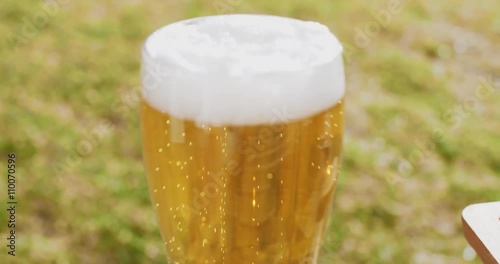 Close up on the mid section of a glass of refreshing ice cold beer or lager with a frothy top served outdoors in the garden on a summer picnic. photo