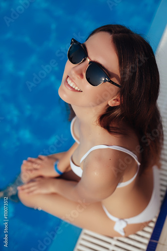 Tanned beautiful woman in white bikini and sunglasses sitting ne