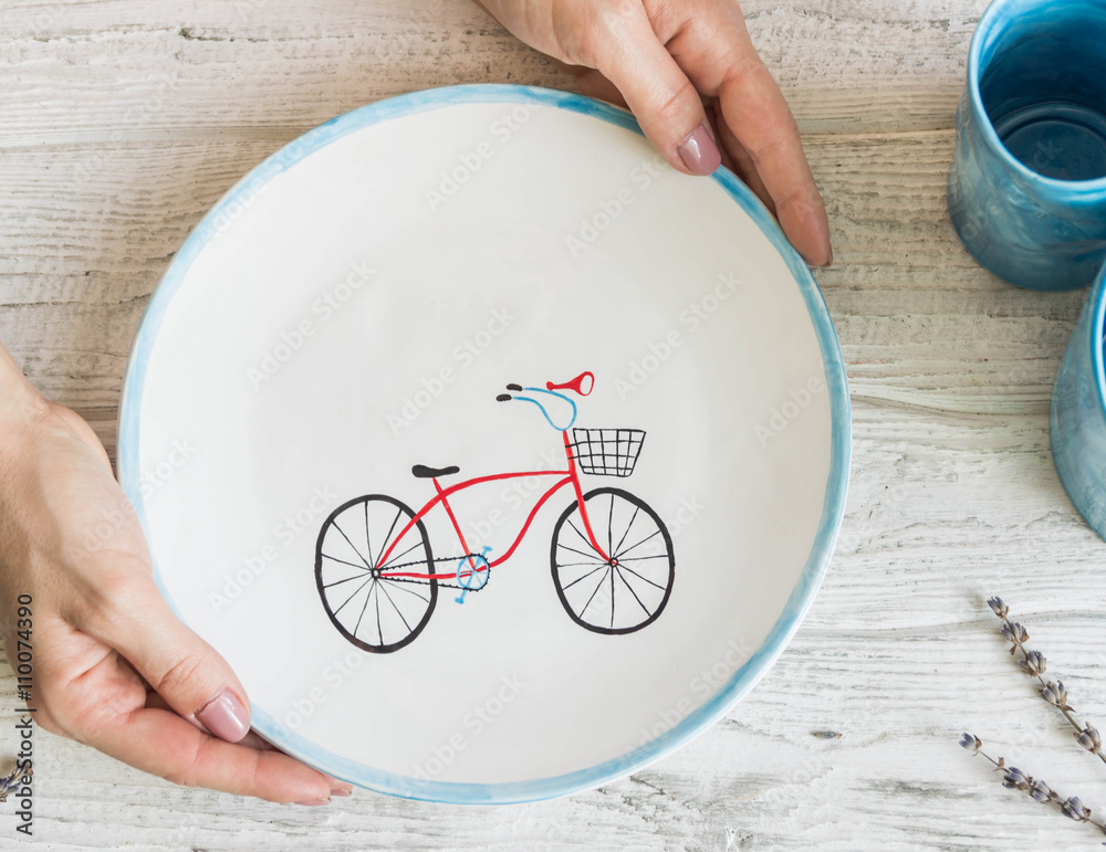 Ceramic handmade plate with a painted bike. Hands in the frame. Copyspace