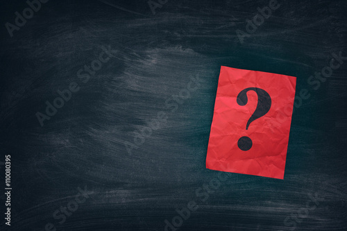 Red paper note with question marks on black board