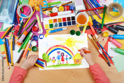 family on meadow with rainbow and house child drawing  top view hands with pencil painting picture on paper  artwork workplace