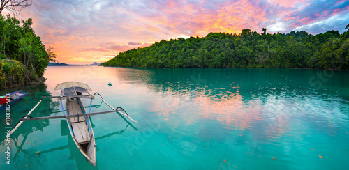 Canvas Print Breathtaking colorful sunset and traditional boat floating on scenic blue lagoon in the Togean (or Togian) Islands, Central Sulawesi, Indonesia, upgrowing travel destination