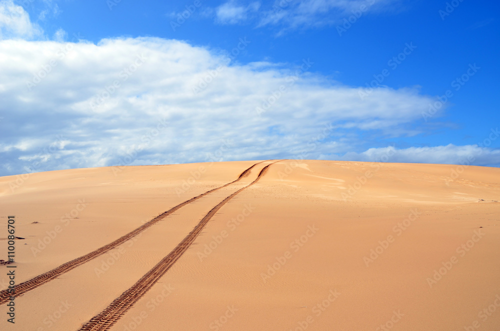 Tracks in remote sand dunes under blue skies