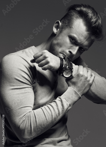 Advertising wrist watch concept. Beautiful (handsome) muscular male model with perfect body in grey jumper. He bites and unfastens the bracelet from the clock. Street style. Black and white 