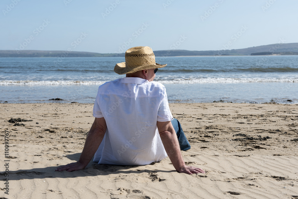 Rear view on a casual mature man sitting on the beach on a sunny day. 