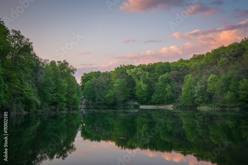 Green forest, a lake and a sunset sky with pink clouds